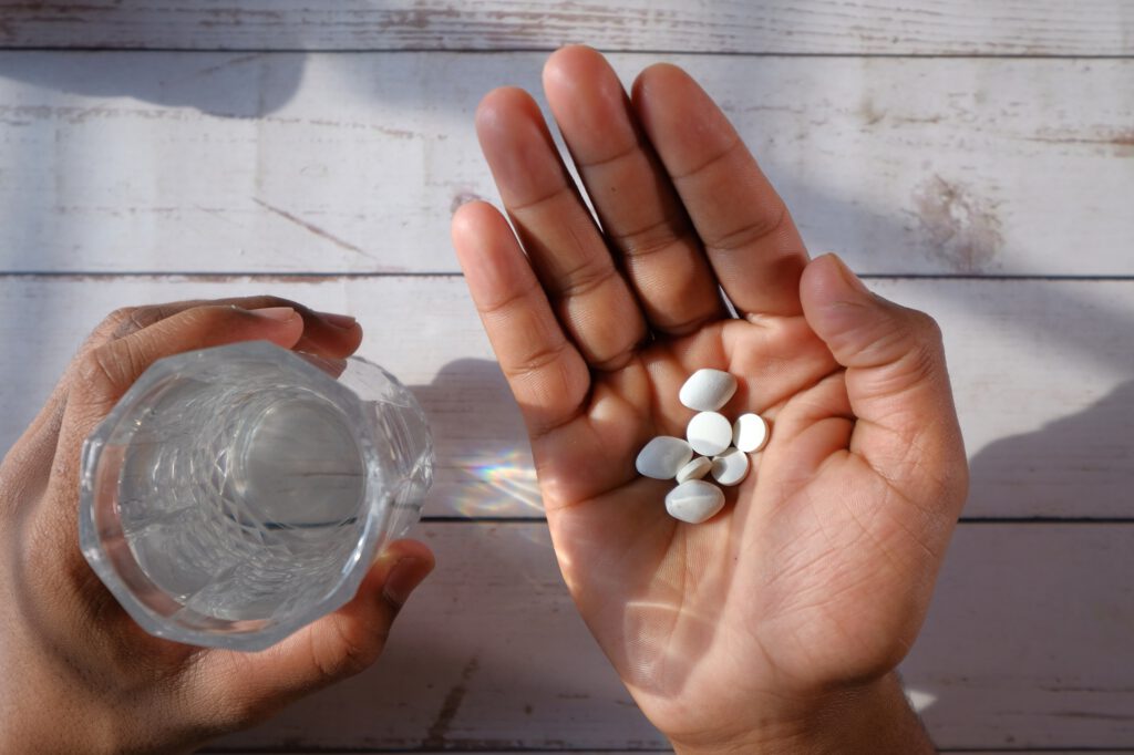 A person is holding various pills along with a glass of water on a wooden surface