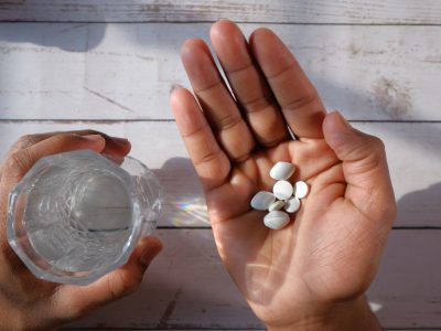 A person is holding various pills along with a glass of water on a wooden surface